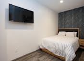 Thumbnail 19 of 20 - A bedroom with a bed, nightstand, and a flat screen TV mounted on the wall.