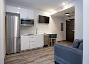 Thumbnail 11 of 20 - A modern kitchen with a grey couch and a TV mounted on the wall.