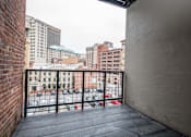 Thumbnail 2 of 20 - A balcony with a black railing overlooks a parking lot and buildings.