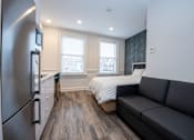Thumbnail 7 of 20 - A modern kitchen with a refrigerator on the left and a grey couch in the middle of the room.