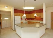 Thumbnail 12 of 37 - A kitchen with a white island and brown cabinets.