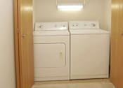 Thumbnail 22 of 37 - A pair of white front loading washing machines in a small laundry room.