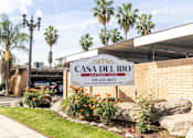 Thumbnail 1 of 38 - A sign for Casa Del Rio Apartment Homes is displayed in front of a building.