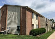 Thumbnail 9 of 18 - A building with a grey and brown exterior and a green bush in front.