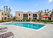 Thumbnail 22 of 28 - a swimming pool with chaise lounge chairs and umbrellas in front of an apartment complex