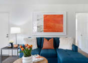 Thumbnail 19 of 38 - a living room with a blue couch and orange artwork