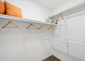 Thumbnail 30 of 38 - a spacious closet with white walls and white hangers with orange pillows on top