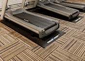 Thumbnail 20 of 24 - Three treadmills are lined up in a row in a room with concrete walls.