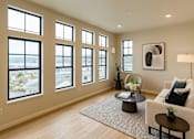 Thumbnail 18 of 24 - A living room with a white couch, a coffee table, and a large window overlooking a cityscape.