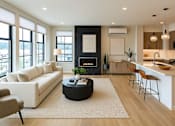 Thumbnail 6 of 24 - A modern living room with a fireplace and a kitchen area.