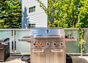 Thumbnail 11 of 21 - A stainless steel outdoor grill with four burners and two ovens is on a patio.