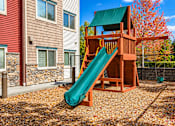 Thumbnail 12 of 21 - A wooden playset with a green slide in front of a red house.