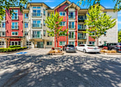 Thumbnail 19 of 21 - A multi-story apartment building with cars parked in front.