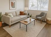 Thumbnail 6 of 11 - A living room with a grey couch, a grey armchair, a coffee table, and a potted plant.