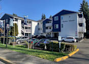 Thumbnail 13 of 13 - A Burien Manor apartment complex with a parking lot in front.