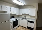 Thumbnail 8 of 16 - A white kitchen with a stove, sink, and cabinets.