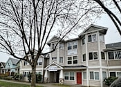 Thumbnail 15 of 16 - A grey house with a red door is in front of a tree.