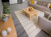 Thumbnail 13 of 21 - A modern living room with a grey sofa, wooden coffee table, and a kitchen area in the background.