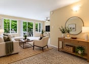 Thumbnail 7 of 15 - A living room with a white couch, a coffee table, a chair, a TV, and a plant.