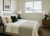 Thumbnail 4 of 16 - A bedroom with a bed, nightstand, and a window with blinds.