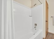 Thumbnail 12 of 14 - A white bathtub with a shower curtain and a towel hanging on the door.