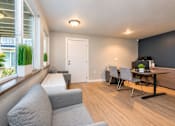 Thumbnail 15 of 18 - A living room with a grey couch, a black table, and a white door.