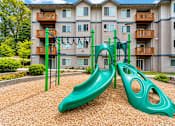 Thumbnail 11 of 18 - A green playground slide in front of a building.