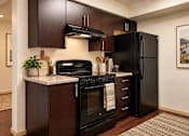Thumbnail 9 of 18 - A black refrigerator is in a kitchen with a stove and oven.