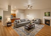 Thumbnail 8 of 18 - A living room with a grey couch, a coffee table, and a fireplace.