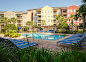 Thumbnail 34 of 42 - a swimming pool with blue lounge chairs in front of an apartment building