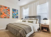 Thumbnail 14 of 42 - A bedroom with a bed, nightstand, and two paintings on the wall.