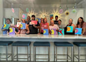 Thumbnail 23 of 37 - a group of people standing in front of a table with paintings on it