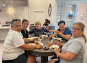 Thumbnail 20 of 37 - A group of people are sitting around a table eating food.