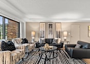 Thumbnail 2 of 12 - A living room with a black and white striped sofa, a black leather chair, and a coffee table with a glass top.