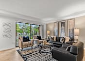 Thumbnail 1 of 12 - A living room with a black couch, a coffee table, and a large window.