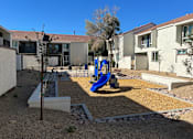 Thumbnail 13 of 20 - A playground with a blue slide in the middle of a gravel area.