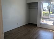 Thumbnail 19 of 20 - A room with wooden flooring and a window showing a view of a parking lot and trees.