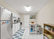 Thumbnail 3 of 19 - A kitchen with a refrigerator, a table, and a bookshelf.