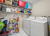 Thumbnail 14 of 19 - A laundry room with two washing machines and a shelf with various items.