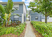 Thumbnail 4 of 16 - A pathway leads between two grey houses surrounded by greenery.