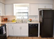 Thumbnail 10 of 28 - A black refrigerator stands in a kitchen with white cabinets.