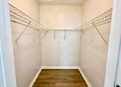 Thumbnail 4 of 16 - A walk-in closet with white walls and wooden floors.