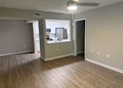 Thumbnail 45 of 75 - A room with a ceiling fan and light fixture, and a kitchen area with a stove and refrigerator in the background.