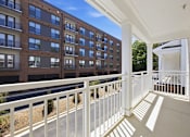 Thumbnail 17 of 63 - A balcony with white railings overlooks a parking lot and a building.