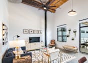 Thumbnail 1 of 8 - A living room with a dark blue sofa, a wooden coffee table, and a TV on the wall at Judson Mill Lofts, South Carolina 29611