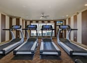 Thumbnail 14 of 14 - a gym with four treadmills and a ceiling fan