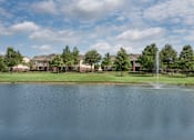 Thumbnail 2 of 14 - a fountain is in the middle of a pond in front of some apartments