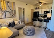 Thumbnail 8 of 21 - A living room with a grey couch, a yellow lamp, and a painting on the wall.