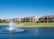 Thumbnail 2 of 21 - A fountain in the middle of a lake in front of a row of houses.