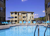 Thumbnail 3 of 16 - a swimming pool with blue chairs and a building in the background